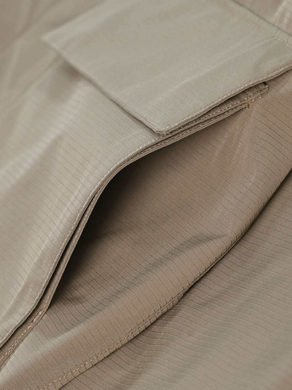 Detail du tissu ripstop beige d'une veste, poche a rabat et coutures apparentes