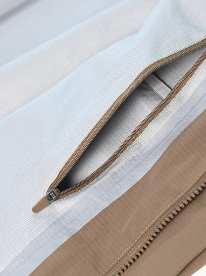 Detail d'une poche zippee sur tissu bleu clair, panneau beige et fermeture marron